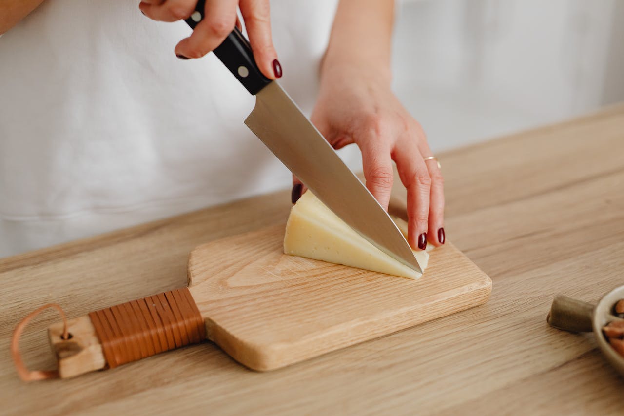 Person Slicing Cheese on Chopping Board