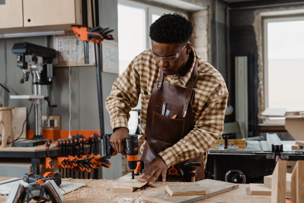 Man in Plaid Long Sleeves Drilling the Wood